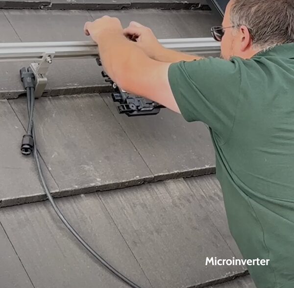 A man fitting a microinverter and mounting rail on a slate-tiled roof for a solar panel installation