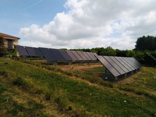 Ground-mounted solar panel array on a grassy slope beside a house