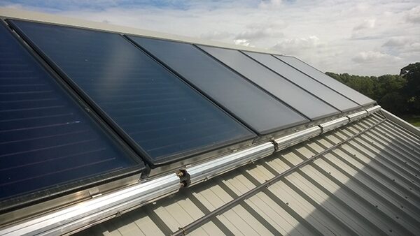 A row of flat-plate solar thermal collectors mounted on a corrugated metal roof.