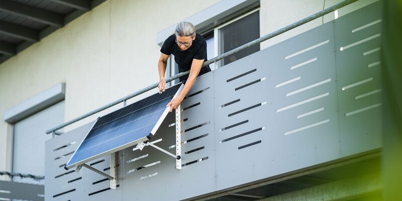 A woman mounting a plug-in solar panel on a balcony railing of an apartment building