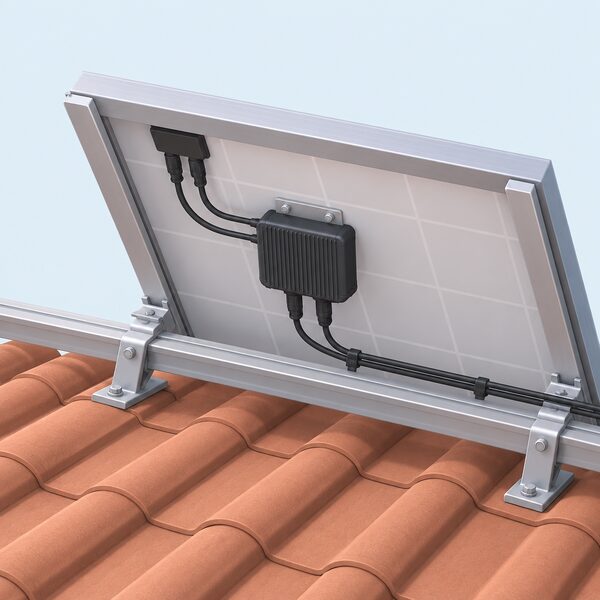 A small rectangular power optimiser unit mounted on the underside frame at the back of a single solar panel on a roof, with short cables connecting it to the panel leads and to the string wiring running along the roof.