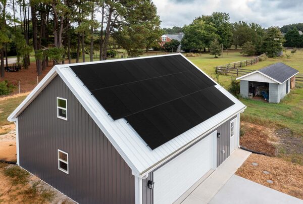 Black solar panels installed on the roof of a grey garage in a rural garden