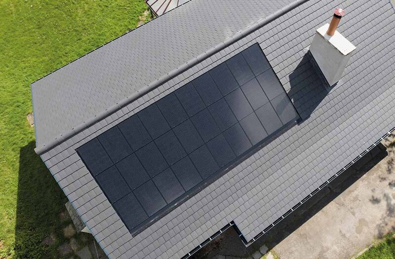 An aerial view of a grey slate roof with a large in-roof solar panel array installed flush with the tiles beside a chimney