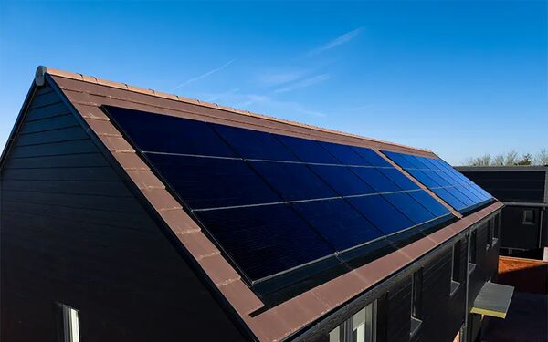 Roof-integrated solar panels installed on the tiled roof of a modern dark-clad house under a blue sky