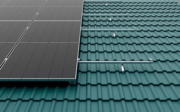 Solar panels and aluminium mounting rails being fitted on a green tiled roof