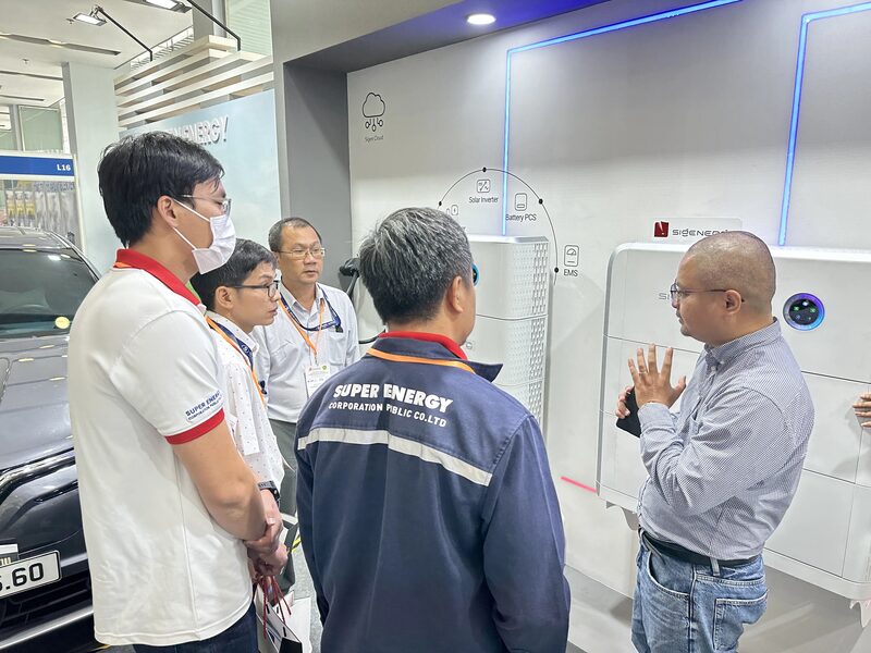 Visitors at a trade exhibition stand looking at Sigenergy home battery and solar inverter products while a representative explains them