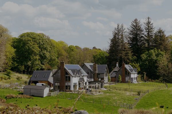 A rural house with solar panels on the roof surrounded by trees and fields