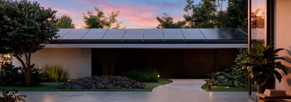 A modern single-storey house with solar panels covering its flat roof at dusk