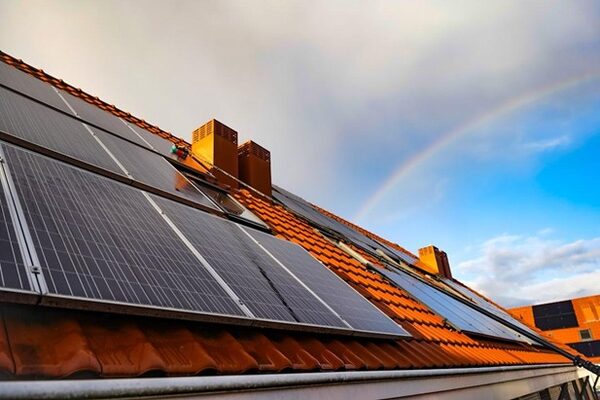 Solar panels installed on a terracotta-tiled roof with a rainbow in the sky behind