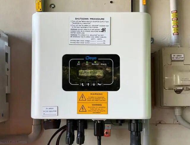 A Deye hybrid solar inverter mounted on a wall with warning labels and DC isolator switches
