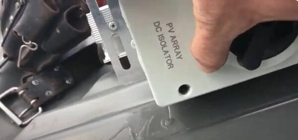 A close-up of a hand operating a PV array DC isolator switch mounted on a wall