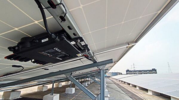 An APsystems microinverter unit mounted on the underside of solar panels on a large rooftop array
