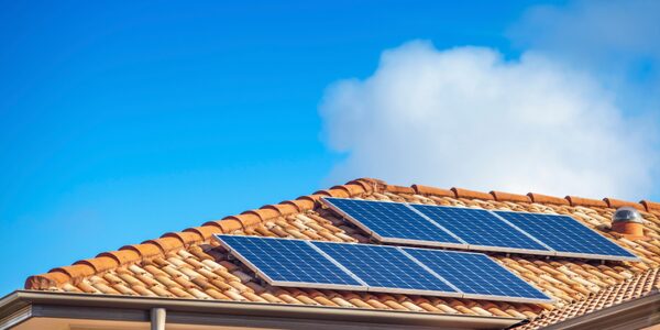 Solar panels installed on a terracotta-tiled domestic rooftop under a blue sky