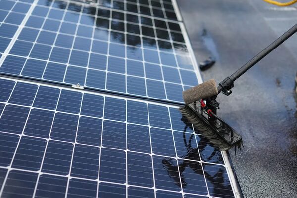 A long-handled rotating brush cleaning wet solar panels on a roof