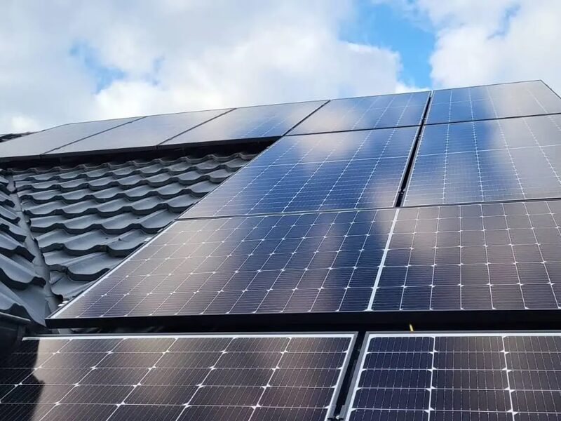 A rooftop solar panel array installed on a tiled roof under a partly cloudy sky