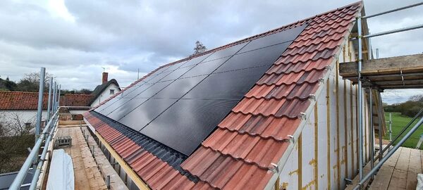 Solar panels being installed on a red-tiled pitched roof of a house surrounded by scaffolding