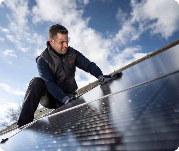 An installer in safety glasses fitting a solar panel on a roof under a blue sky