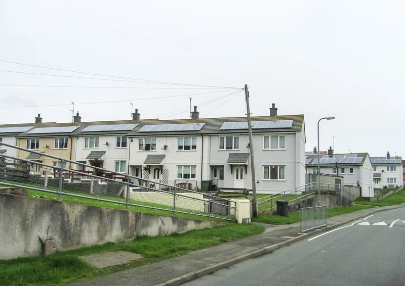 A row of UK terraced houses with rooftop solar panels beside a road