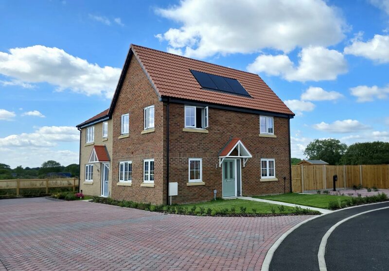 A new-build semi-detached brick house with solar panels on its tiled roof, on a residential street