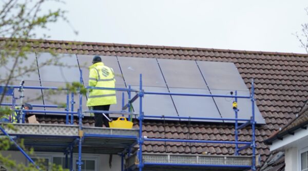 A worker in a high-visibility jacket on scaffolding installing solar panels on a tiled house roof