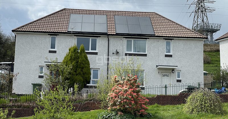 A semi-detached house with solar panels on its tiled roof, with a pylon in the background