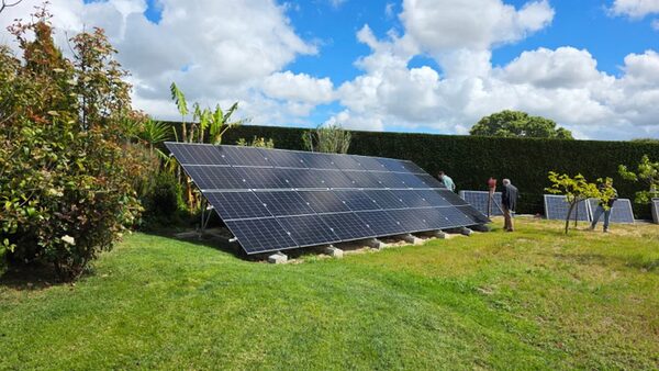 Ground-mounted solar panels being installed in a grassy garden with hedges and trees, with workers nearby