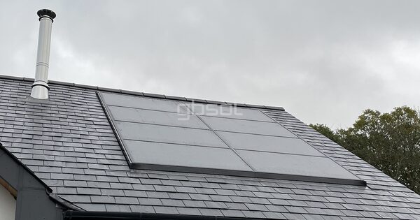 A grey solar panel array integrated into the slate roof of a house next to a stainless flue pipe