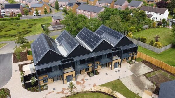 An aerial view of a modern housing development with solar panels covering the dark pitched roofs