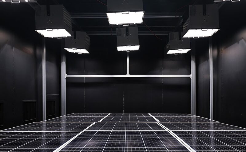 Solar panels lying under bright test lamps in a dark factory testing chamber