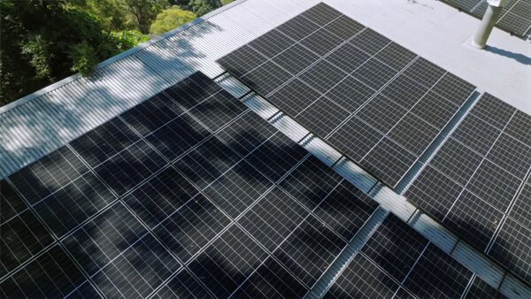 Rooftop solar panels installed on a corrugated metal roof, partly shaded by overhanging trees