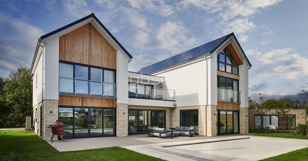 A modern new-build house with solar panels on the roof, timber cladding and a patio by a pool