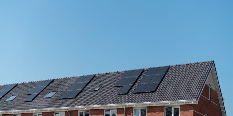 Black solar panels installed on the tiled roof of a brick terraced house against a clear blue sky