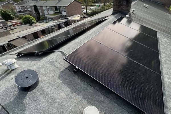 Solar panels mounted low on a flat bitumen roof using a low-profile mounting system, with residential rooftops in the background