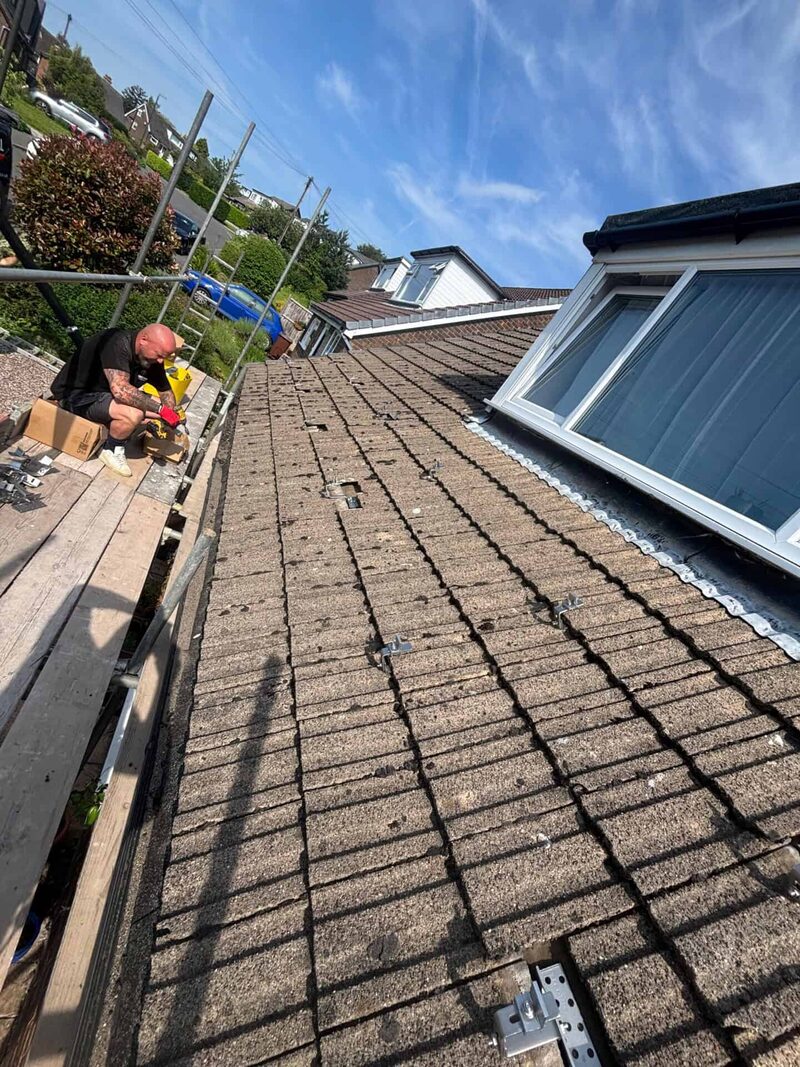A roofer on scaffolding working on a tiled house roof with solar panel mounting brackets fitted under the tiles