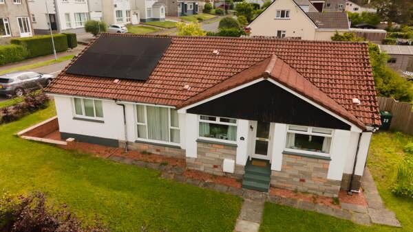 Aerial view of a bungalow with solar panels on its tiled roof in a residential street