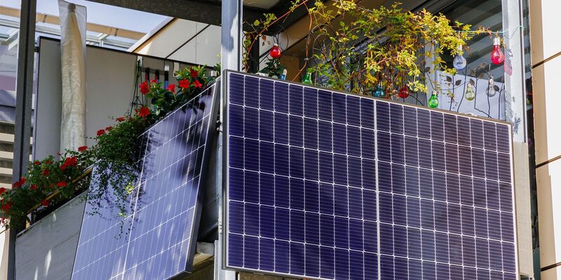 Two plug-in solar panels mounted on a balcony railing with flowers and decorative bulbs