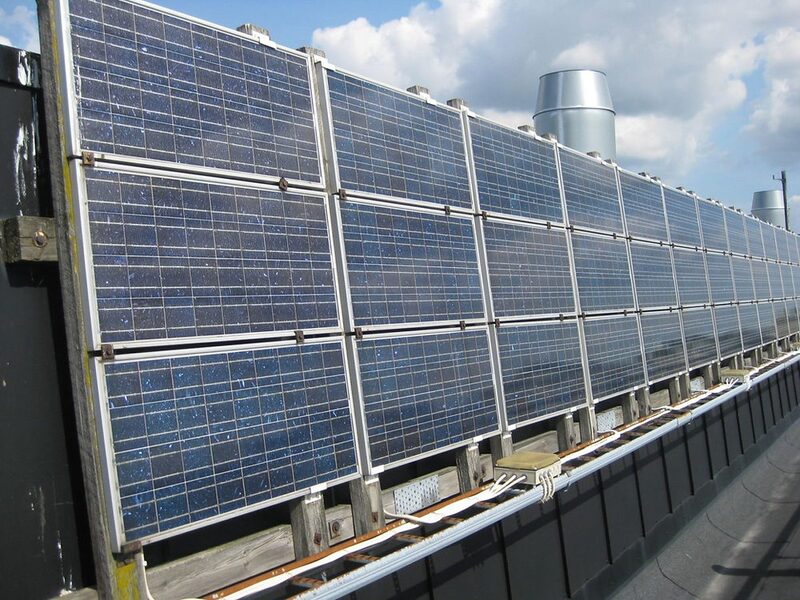 A row of solar PV panels mounted on a flat roof with visible cabling and mounting frames