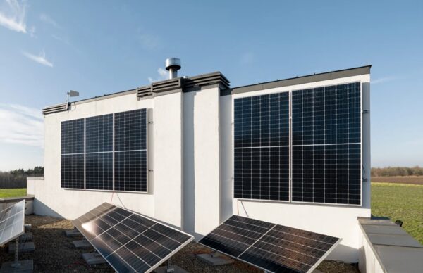 Solar photovoltaic panels mounted on the walls and roof of a white building against a blue sky