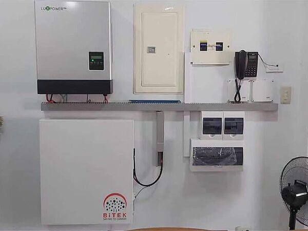 A LuxPower solar inverter and a BITEK battery mounted on a wall alongside consumer units and a telephone, in an indoor electrical installation