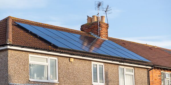 Solar panels installed on the tiled roof of a brick terraced house with a chimney and TV aerials