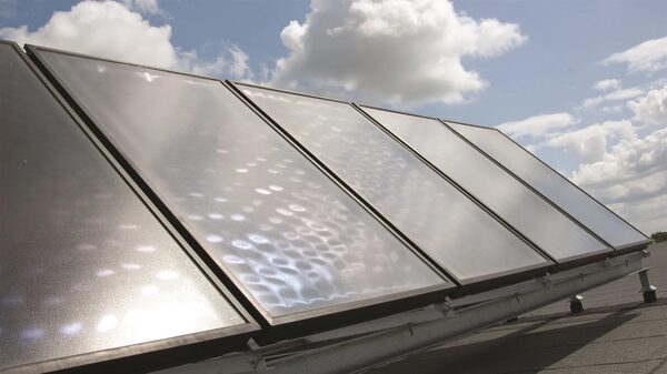 A row of solar thermal panels mounted on a flat roof under a partly cloudy sky