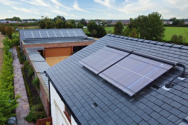 Aerial view of a slate-roofed house with evacuated tube solar thermal collectors and a neighbouring building with flat solar panels in the countryside