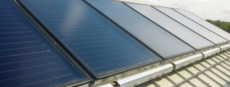 A row of flat-plate solar thermal collector panels mounted on a corrugated metal roof