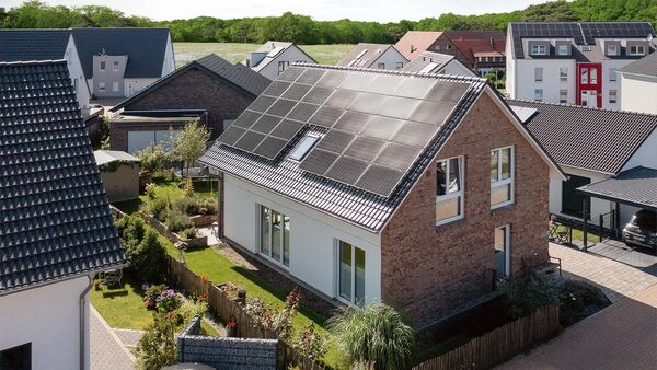A brick single-family house with a large solar panel array covering its pitched roof, in a suburban neighbourhood