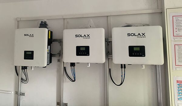 Three white SolaX Power wall-mounted battery inverters installed on a metal frame against a wall