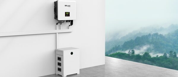 A SolaX three-phase hybrid solar inverter mounted on a white wall above a SolaX battery unit, with a misty forest landscape in the background