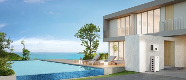 A SolaX home battery storage unit and inverter mounted on the wall of a modern luxury villa beside a swimming pool overlooking the sea