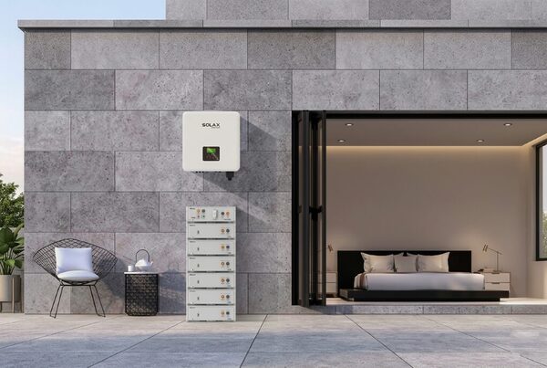A SolaX wall-mounted inverter and stacked battery modules installed on the exterior wall of a modern house beside an open bedroom