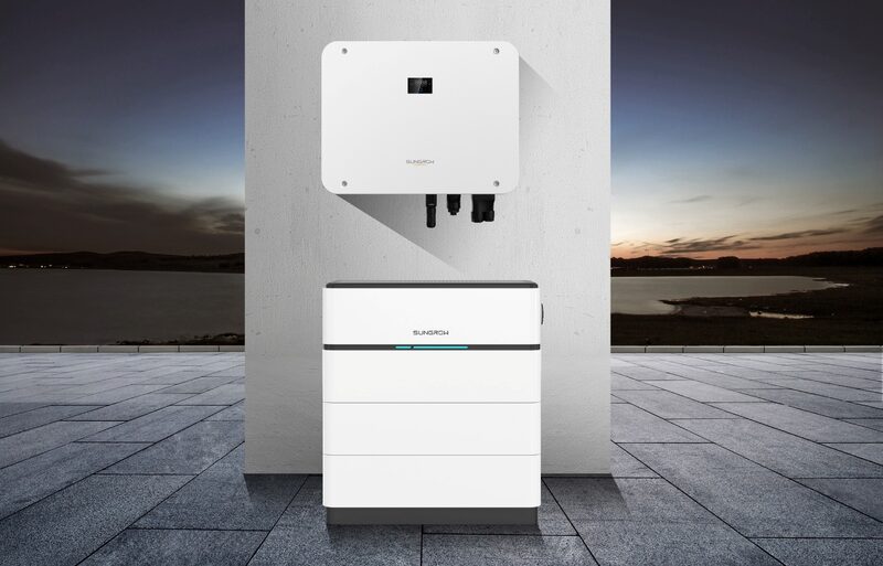 A Sungrow hybrid inverter mounted on a wall above a stacked Sungrow home battery, shown against a rendered sunset backdrop