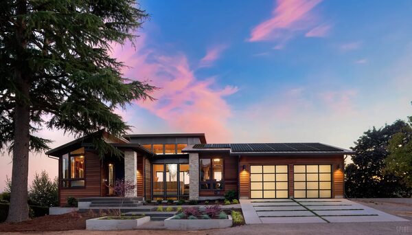 A modern timber-clad house with solar panels on the roof at sunset